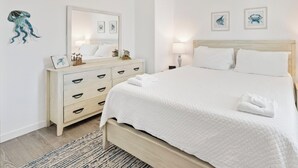 A clean, white bedroom with a bed, bedside tables, a ceiling fan, and wall art. - Coastal Getaway | Heated Pool, Water Slides & Beach Nearby (Corpus Christi)