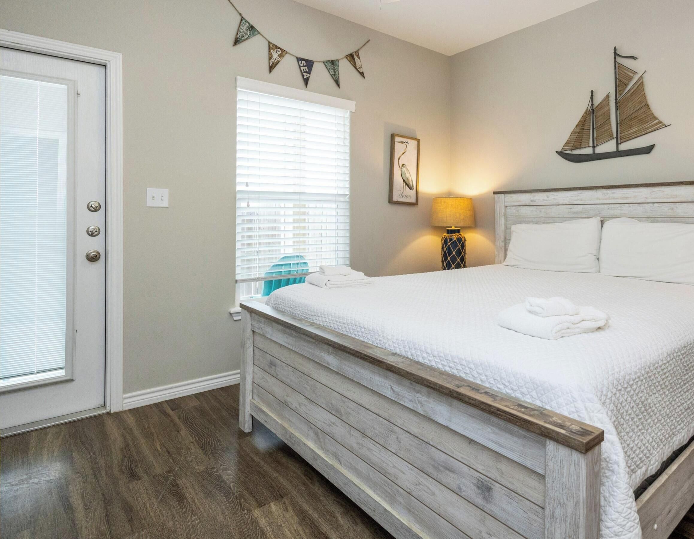 A bedroom with a wooden bed, a window with blinds, a lamp, and a sailboat decoration on the wall.