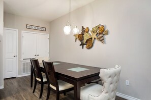 Un comedor con una mesa y sillas de madera, un adorno en la pared y un cartel que dice "BEACH HOUSE".
