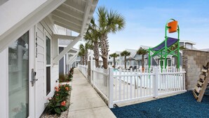 A row of beach houses with a white fence, palm trees, and a play structure.