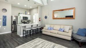 A modern kitchen with a central island, a dining area with bar stools, a large mirror, and a sofa with patterned cushions.