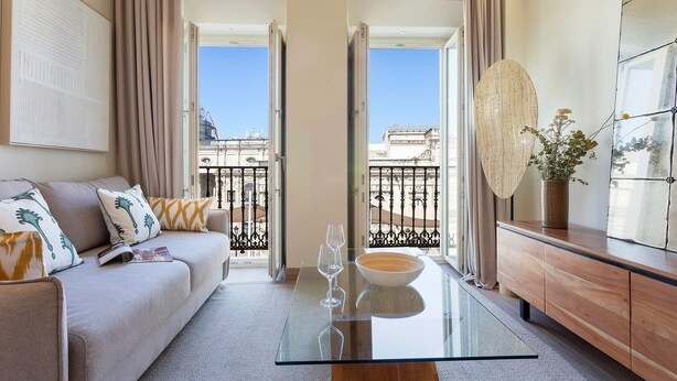 A modern living room with a glass coffee table, a sofa with patterned cushions, a wooden cabinet, and a view of the cityscape through open doors. - Genteel Home San Francisco III (Seville)