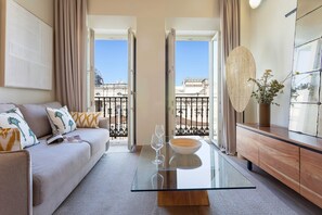 A modern living room with a glass coffee table, a sofa with patterned cushions, a wooden cabinet, and a view of the cityscape through open doors. - Genteel Home San Francisco III (Seville)