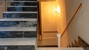 Una escalera con peldaños de mármol y barandillas de madera, que conduce a un rellano con una lámpara.