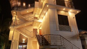 A multi-story building with a central staircase, multiple balconies, and a well-lit entrance. - Diamond Residency (Ambalapuzha)