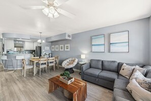 Un salon moderne avec un canapé gris, une table basse en bois et un coin repas comprenant une table et des chaises blanches.
