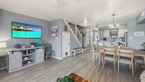 Un salón amplio con televisor, una mesa de comedor de madera y una escalera que lleva a la cocina.