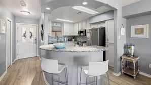 Una cocina con una isla curva, taburetes blancos para bar y un refrigerador.