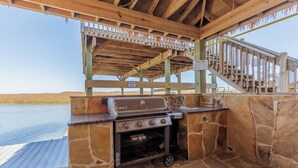 An outdoor grill area with a stone wall, a wooden deck, and a view of a body of water.