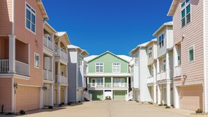 A row of townhouses with a central green house, each with a garage and a balcony.