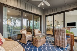 A spacious outdoor area with wicker furniture, a ceiling fan, and a view of the interior through glass doors.