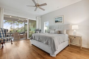A bedroom with a large bed, a ceiling fan, a nightstand, and a view of the outdoors. - 3104 Marsh View - Spacious 2 Bedroom with Amazing Marsh Views (Fernandina Beach)