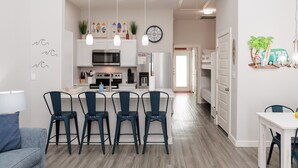 Una cocina moderna con armarios blancos, una isla central con taburetes y luminarias colgantes.