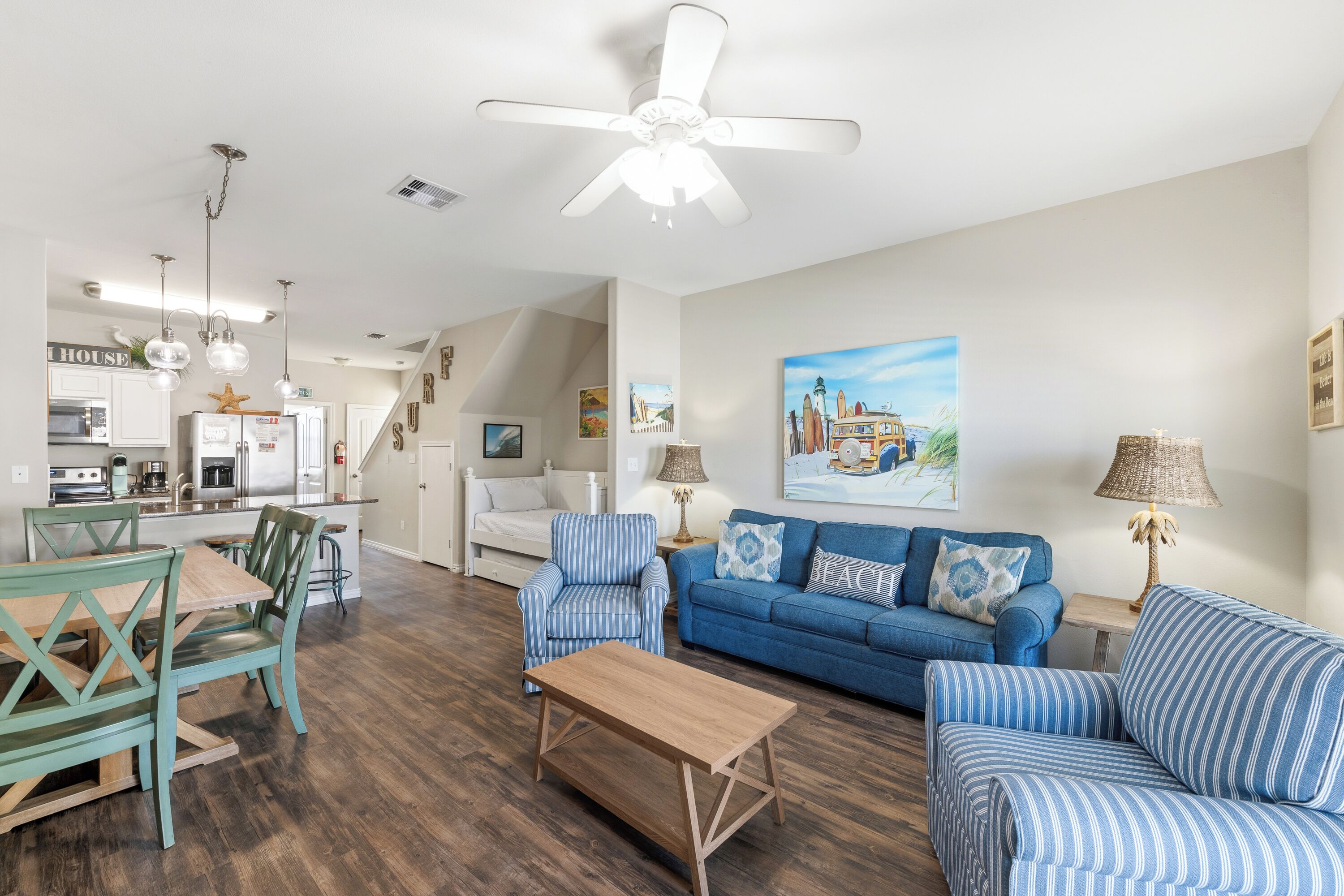 A spacious living room with a blue sofa, a wooden coffee table, and a dining area with chairs and a kitchen in the background.