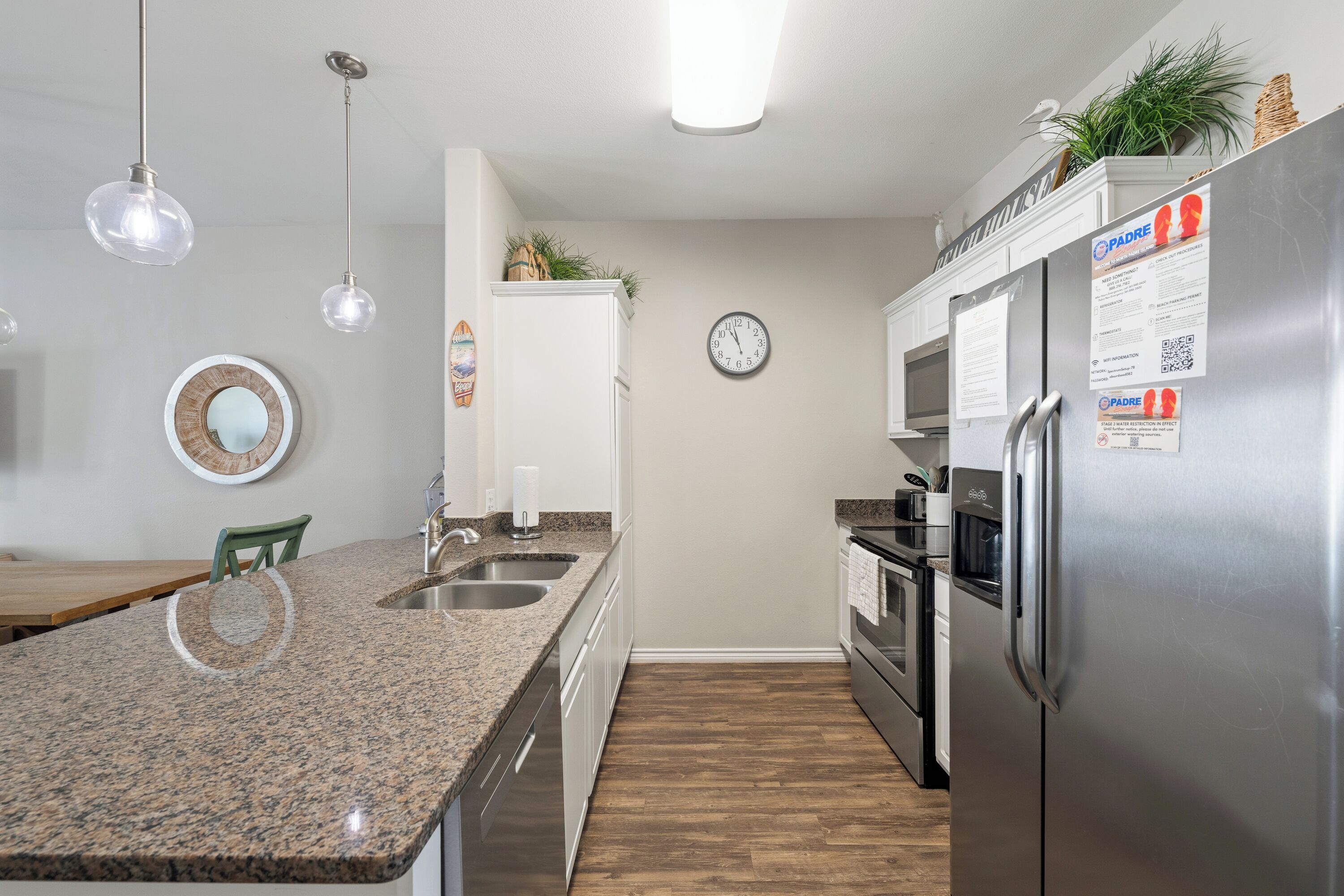 Une cuisine moderne avec des comptoirs en granit, des appareils électroménagers en acier inoxydable et une horloge au mur.