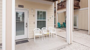 A building entrance with a door labeled "BEACONS," a covered porch with white plastic chairs, and a small balcony with a wooden railing.