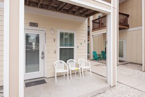 A building entrance with a door labeled "BEACONS," a covered porch with white plastic chairs, and a small balcony with a wooden railing. - Dog-Friendly Townhome | Pool Access, Balcony & Walk to Beach (Corpus Christi)