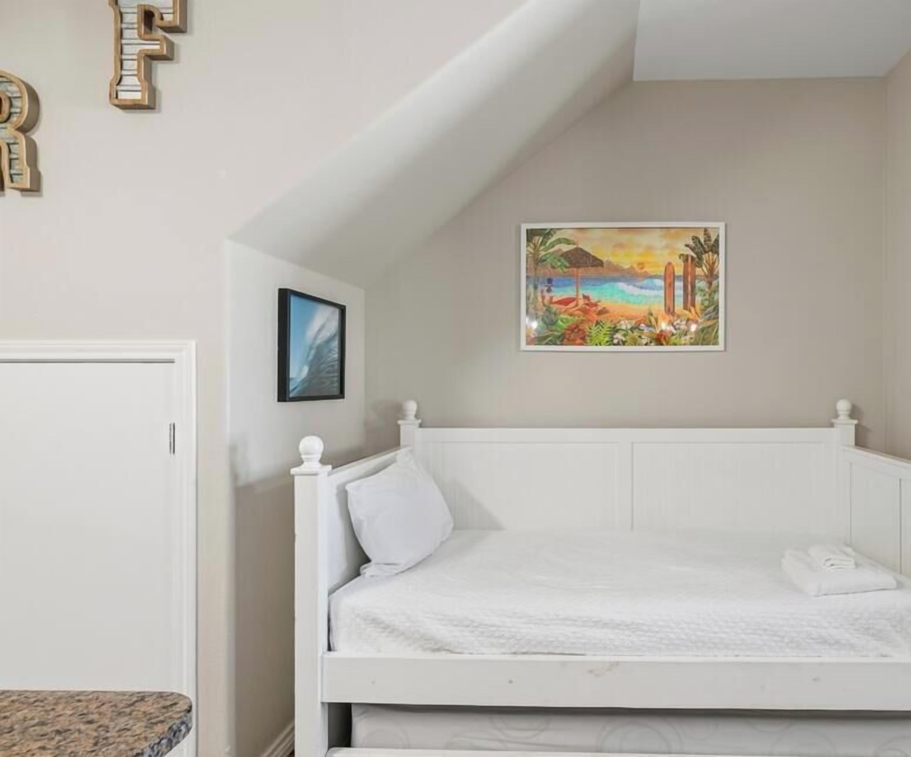 A bedroom with a white bed, a painting of a tropical scene, and a door.