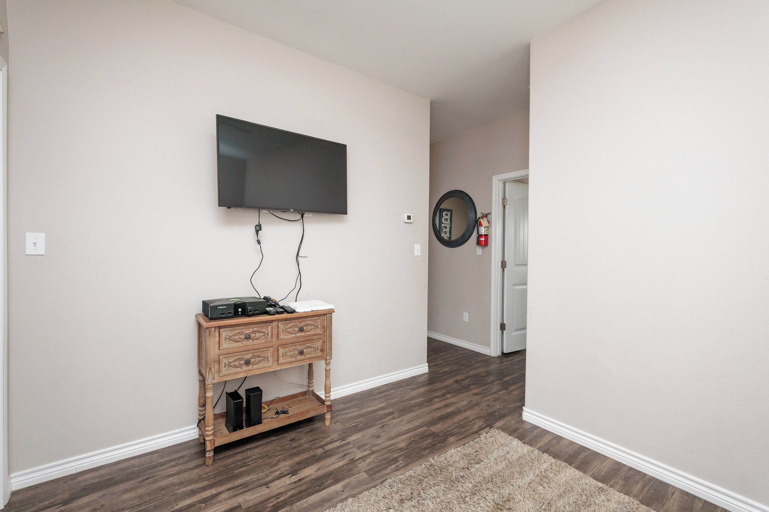 A hallway with a flat-screen TV mounted on the wall, a wooden console table with drawers, a mirror, and a door with a circular mirror above it.