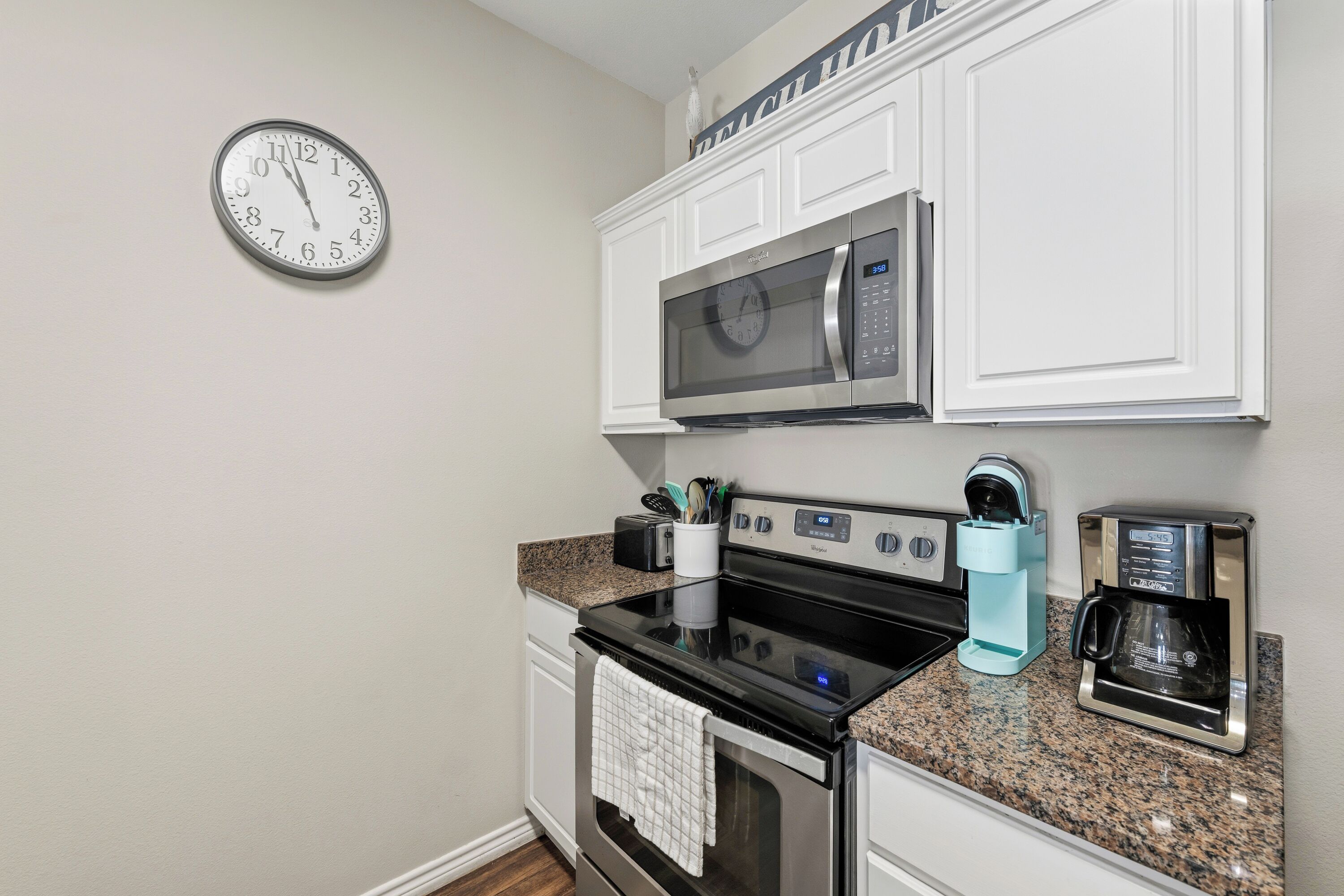 A kitchen with a clock, microwave, stove, and coffee maker.