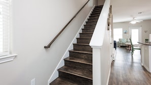 A staircase with dark wooden steps and white handrails, leading to a room with a ceiling fan and a view of a dining area.