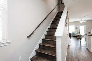 A staircase with dark wooden steps and white handrails, leading to a room with a ceiling fan and a view of a dining area. - Dog-Friendly Townhome | Pool Access, Balcony & Walk to Beach (Corpus Christi)