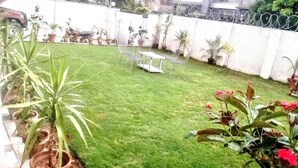 Ein gepflegter Garten mit Rasen, Blumentöpfen, einem Tisch und Stühlen.