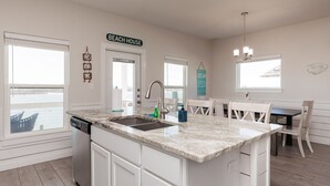 A kitchen with a large island, white cabinetry, a dishwasher, and a sign that reads "BEACH HOUSE". - Pet-Friendly Retreat | 2 Resort Pools, Pickleball & Docks (Corpus Christi)
