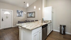 A modern kitchen with a marble countertop, stainless steel appliances, pendant lighting, and a dining area with gray chairs. - Your Perfect Escape | Heated Pools, Pickleball & Resort Amenities (Corpus Christi)