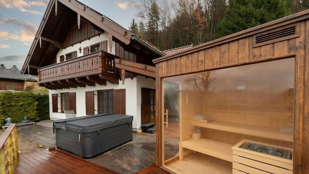 Une terrasse en bois avec un jacuzzi et un espace sauna fermé par des parois de verre.