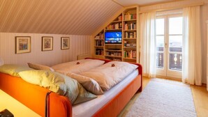 Une chambre confortable avec un plafond en pente, un grand lit, une télévision et une bibliothèque.