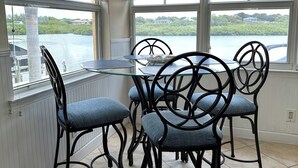 Spiseområde med et glasbord og sorte metalstole, store vinduer med persienner samt udsigt til en sø.