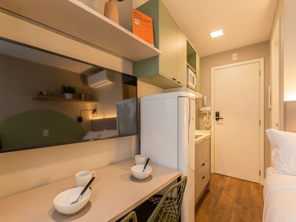 A compact hotel room with a kitchenette, a bed, a bathroom, and a large mirror.