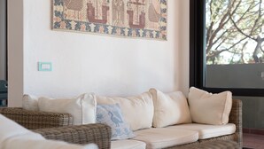 A living room with a beige sofa, a wicker chair, and a patterned tapestry on the wall. - Villa in Sardinia overlooking the sea (Porto Sa Ruxi)