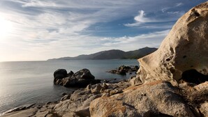 A rocky coastal landscape with a calm sea and distant mountains under a partly cloudy sky. - Villa in Sardinia overlooking the sea (Porto Sa Ruxi)
