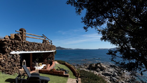 A stone building with a wooden deck and outdoor seating, overlooking a coastal view. - Villa in Sardinia overlooking the sea (Porto Sa Ruxi)