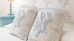 A bed with two pillows featuring a blue tree pattern, a nightstand with a lamp, and a wall with a curtain. - Villa in Sardinia overlooking the sea (Porto Sa Ruxi)