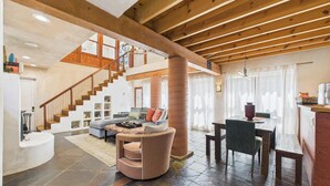 A spacious living area with a wooden ceiling, a staircase, a sofa, a coffee table, and a dining table. - Meticulously Designed Home with Lavish Furnishings (Santa Fe)