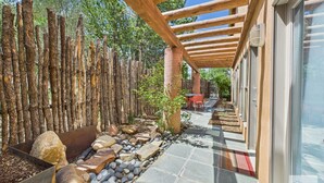 A covered outdoor area with a stone pathway, wooden beams, and a rustic fence. - Meticulously Designed Home with Lavish Furnishings (Santa Fe)