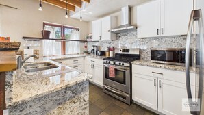 A modern kitchen with white cabinets, granite countertops, stainless steel appliances, and a wooden ceiling. - Meticulously Designed Home with Lavish Furnishings (Santa Fe)