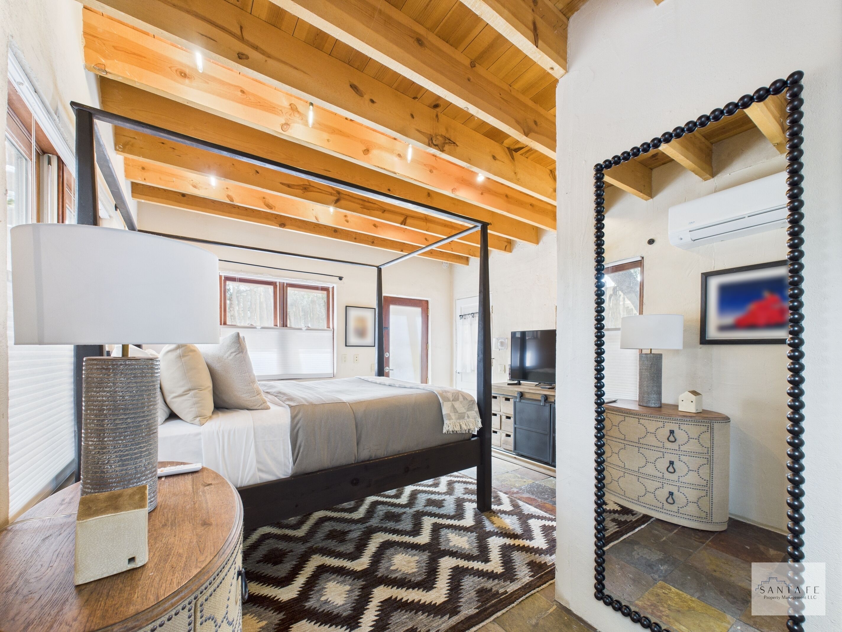 A bedroom with a four-poster bed, a bedside table with a lamp, a dresser, and a patterned rug.