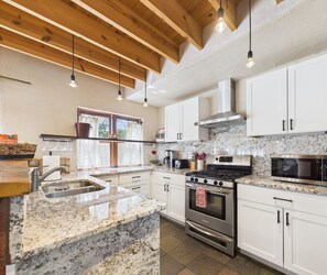 Una cocina moderna con armarios blancos, encimeras de granito, electrodomésticos de acero inoxidable y techo de madera.