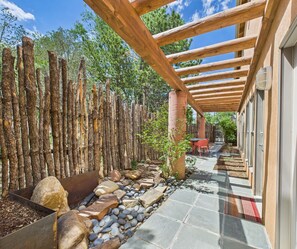 Un espacio al aire libre techado con un sendero de piedra, vigas de madera y una valla rústica.