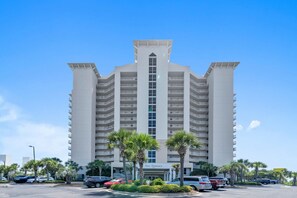 A multi-story hotel with a central atrium, balconies, and palm trees in front. - ⛱️Terrace at Pelican Beach 1102 - Emerald Dreams | Incredible Gulf Views⛱️ (Destin)