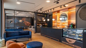 Ein modernes Café mit einem blauen Sofa, orangefarbenen Stühlen, einer Bedientheke und einer Wand mit einer Speisekarte.