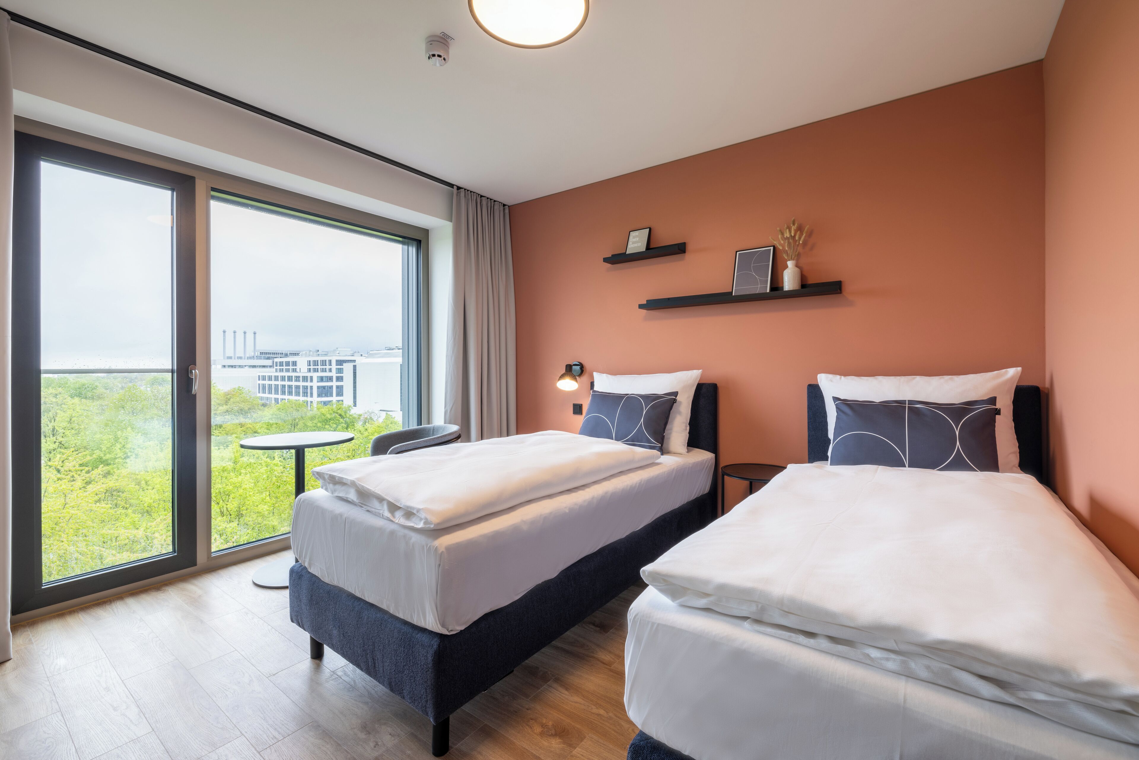 Una habitación de hotel moderna con dos camas, un balcón y vistas a la ciudad, además de una pequeña mesa.