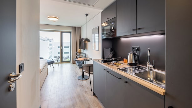 Eine moderne Küche mit integriertem Mikrowellenherd, Wasserkocher und Spüle. Ein Essbereich mit Tisch und Stühlen lädt zum Verweilen ein, und ein großes Fenster bietet Blick auf die Stadt.