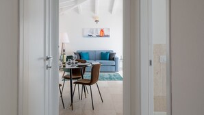 A hallway leading to a dining area with a table set for two, a blue sofa, and a decorative wall piece in the background. - Bellevue 36B by Klodge - flat with pool and views (Budoni)