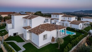 A white villa with multiple rooms, a swimming pool, and a view of the sea.