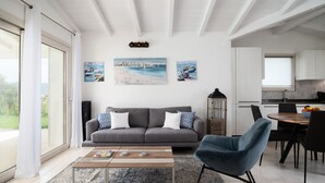 A modern living room with a grey sofa, a blue armchair, and a coffee table. There are two paintings on the wall depicting coastal scenes.